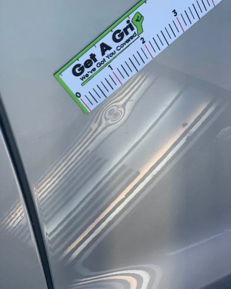 Ruler measuring a dent on a grey panel